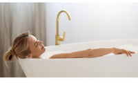 Self-care for moms with mother relaxing in a bathtub in a simple white bathroom.