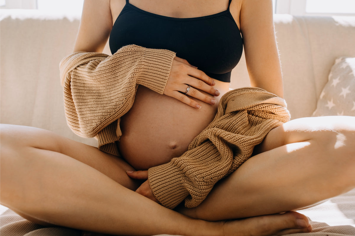 Pregnant woman cradling her belly while sitting in a cozy, sunlit space, embracing motherhood and self-care.