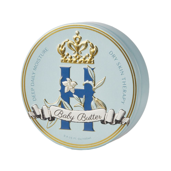 A round cosmetic tin for Baby Butter dry skin therapy, featuring a light blue lid with gold trim, a large blue monogram 'H', a white vanilla orchid flower, and a gold crown on a white background.