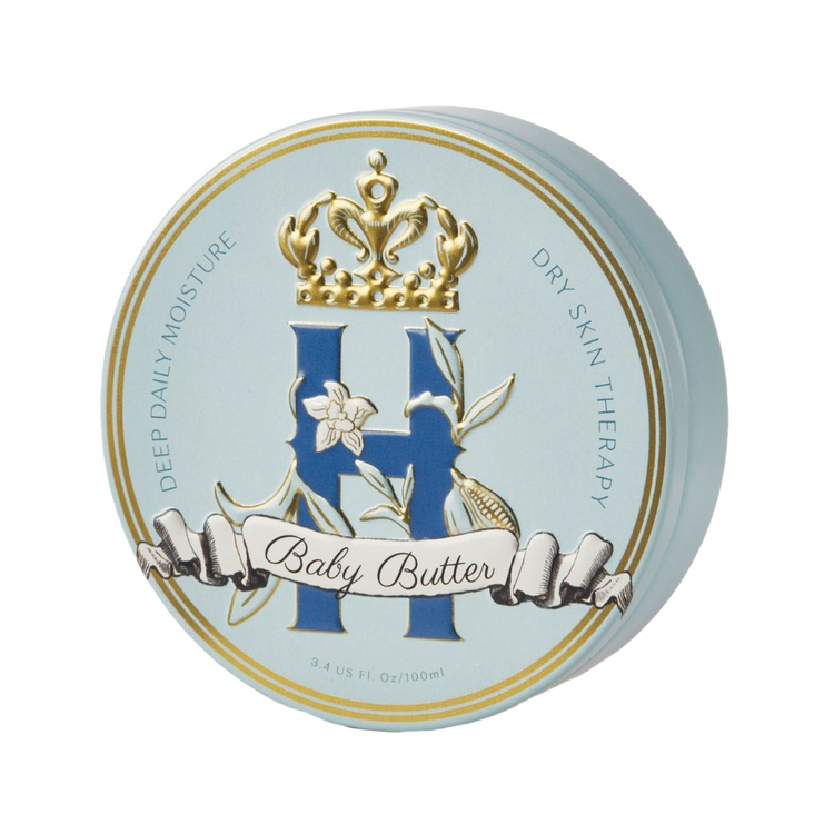 A round cosmetic tin for Baby Butter dry skin therapy, featuring a light blue lid with gold trim, a large blue monogram 'H', a white vanilla orchid flower, and a gold crown on a white background.