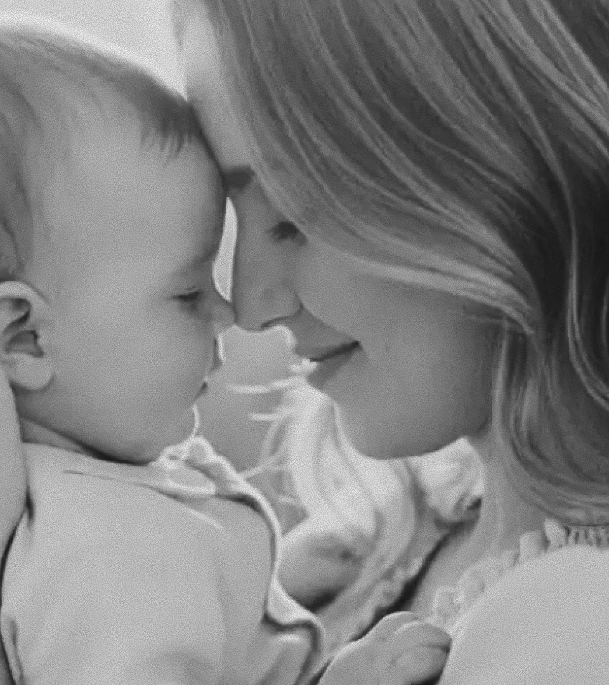 Black and White photograph of a woman holding a baby, their foreheads and noses touching lightly with sunlight backlighting them.