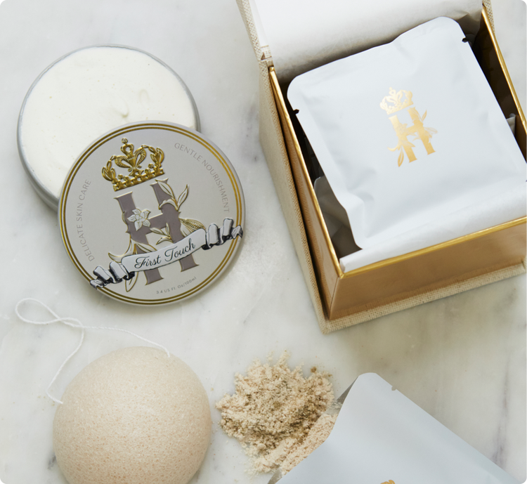 Evening containment ritual by Royal Heir Botanicals is a luxury maternity skincare set for mom and baby featuring a cream coloured cube shaped box for Lavender botanical soak, a round grey and gold tin with First touch whipped organic,EWG verified butter for newborns, konjac sponge with a string and a few white sachets with golden logo on the front with lavender botanical soak on a white marble surface